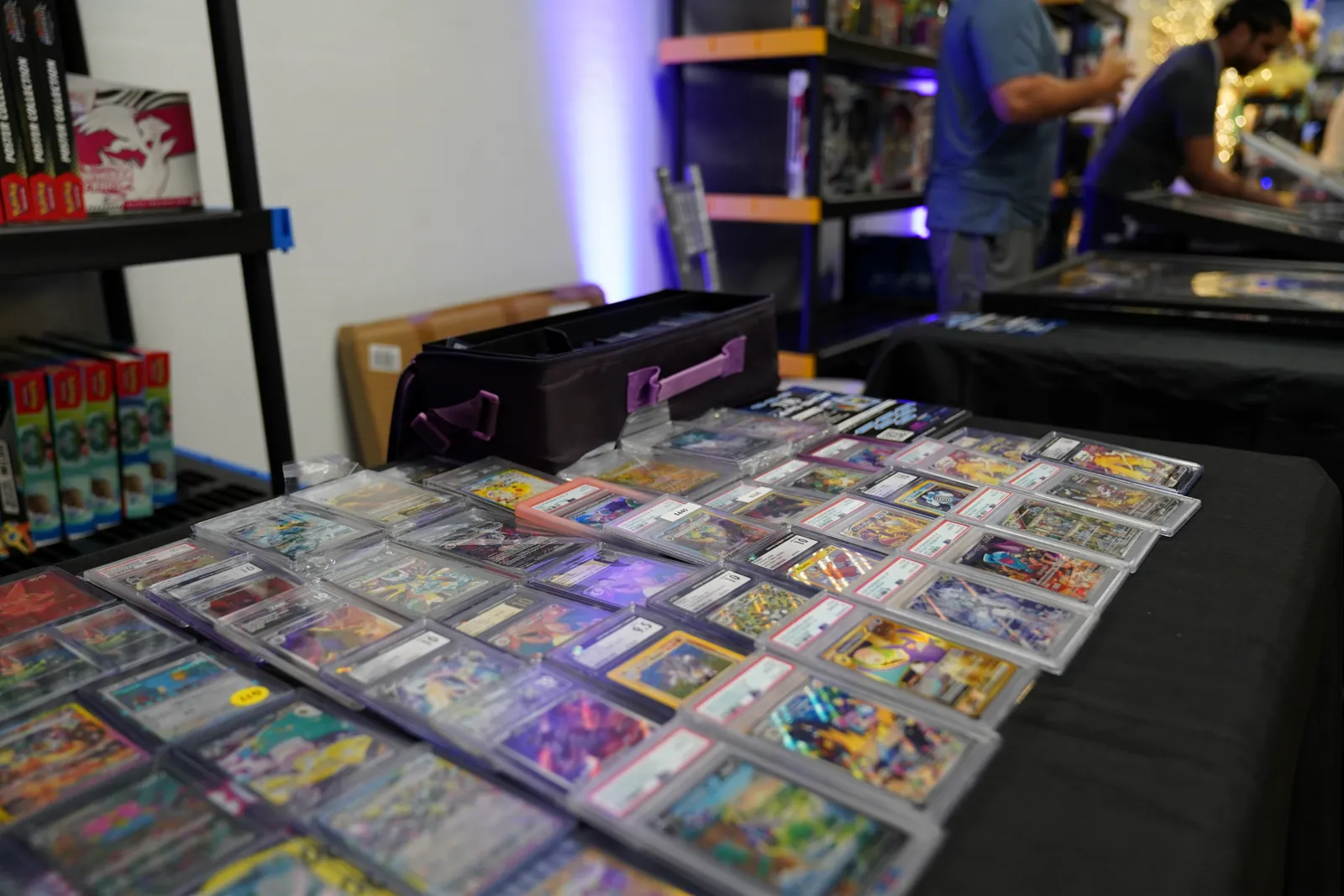 A vendor table spread with graded Pokémon card slabs and a card carrying case
