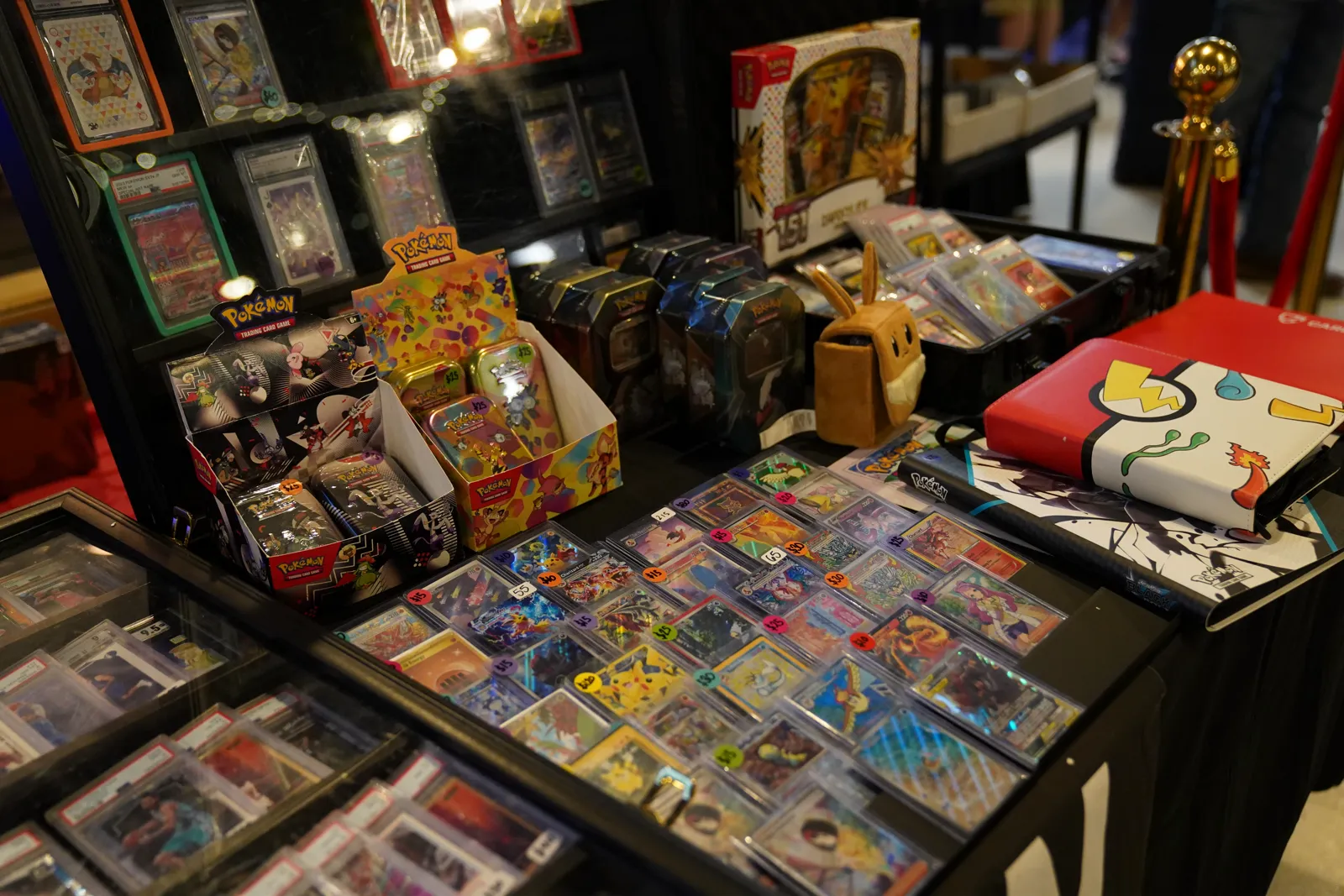 A vendor table with graded cards, Pokémon booster boxes, and plush merchandise