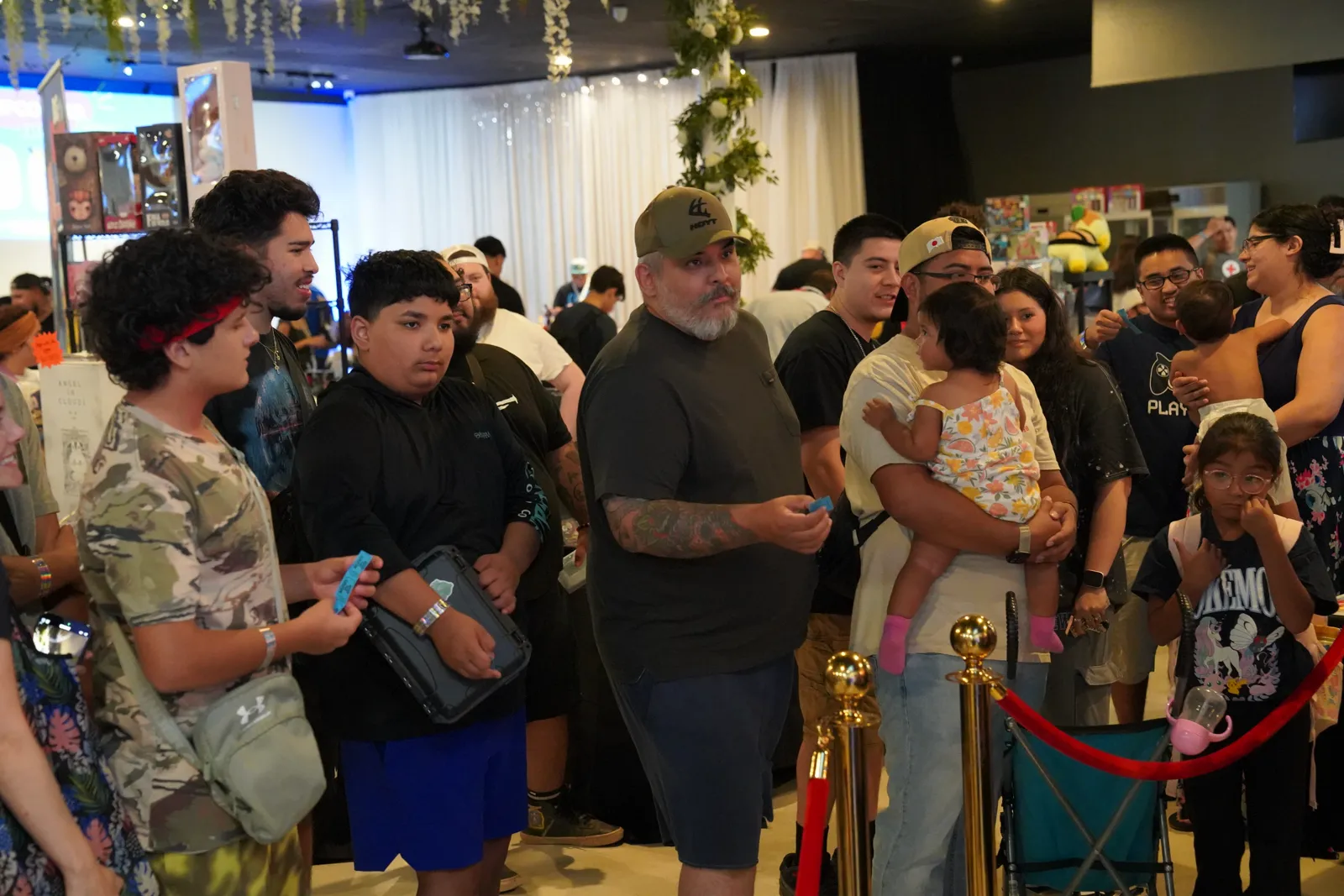 Attendees, including families with kids, gather near the entrance under a floral string-light installation