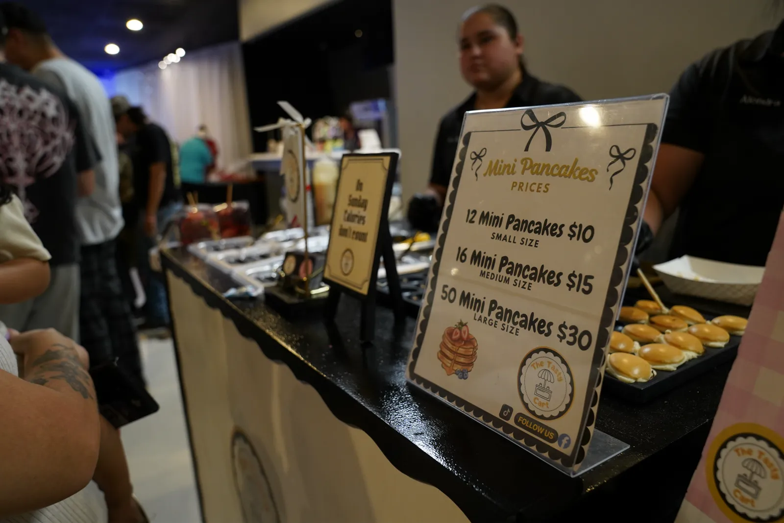 A food vendor's mini pancakes cart with a menu sign and fresh pancake skewers