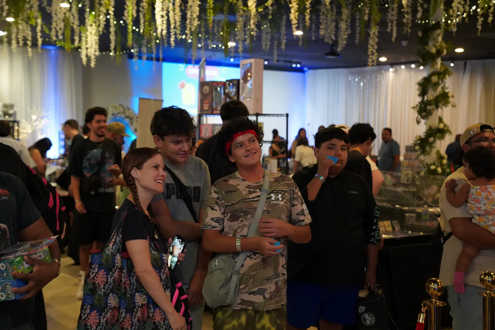 A family browses vendor tables under a hanging floral and string-light display